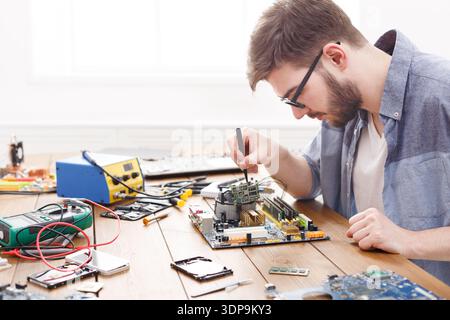 Man Works on Computer Motherboard in Workshop During Daytime Repair Session Stock Photo