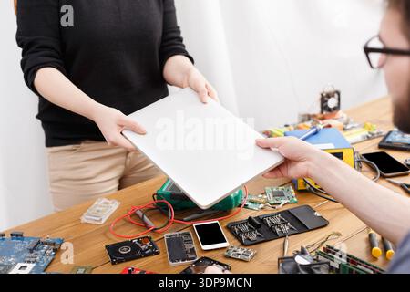 Individual Hands Over a Blank Tablet in a Workspace Filled With Electronics and Tools Stock Photo