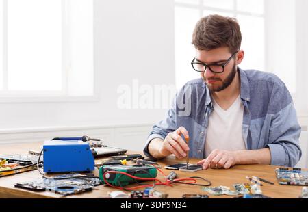Man Repairing Electronic Circuit Boards in a Work Area With Tools and Devices Nearby Stock Photo