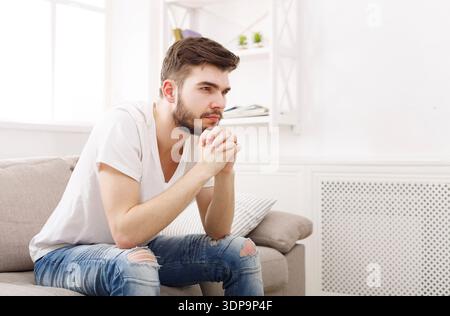 Man Sits on Couch With Hands Clasped, Looking Thoughtful in a Cozy Room Setting Stock Photo