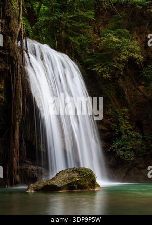 Erawan Falls cascading through lush greenery in Erawan National Park. Tropical forest surrounds the scenic waterfall in Thailand. Stock Photo