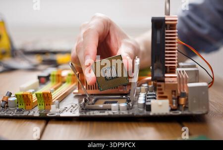 Person Installs CPU Onto Computer Motherboard in Workshop Setting With Tools and Components Stock Photo