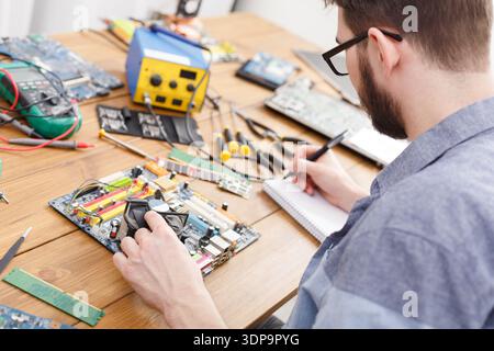 Man Works on Computer Hardware at a Wooden Table With Tools and Parts Around Stock Photo