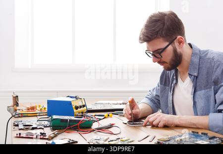 Man Works on Electronic Circuit Board With Tools and Equipment in a Bright Room Stock Photo