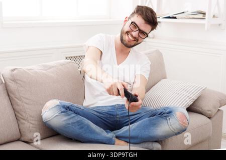 Man Enjoys Gaming at Home While Sitting on a Couch With a Gaming Controller in Hand Stock Photo