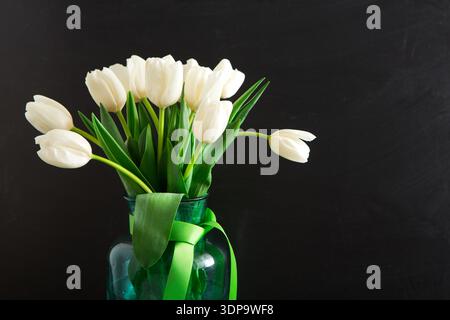 Arrangement of White Tulips in a Green Glass Vase With a Ribbon on a Dark Background Stock Photo
