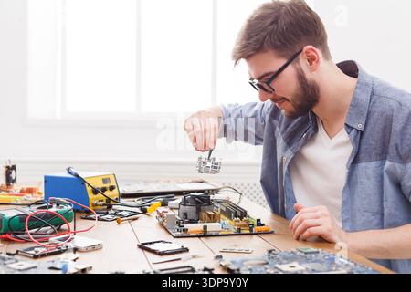 Man Working on Computer Hardware With Tools in a Bright Workspace Stock Photo