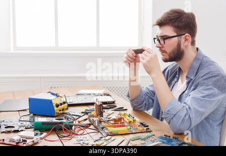 Computer Technician Examines Circuit Board Components in Workshop Setting With Tools Around Stock Photo