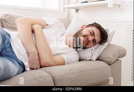 Man Lying on Couch With Stomach Pain in a Bright and Modern Living Room Setting Stock Photo
