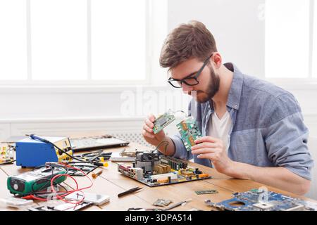 Technician Repairs Circuit Board at Work Table During a Technical Project in a Bright Room Stock Photo