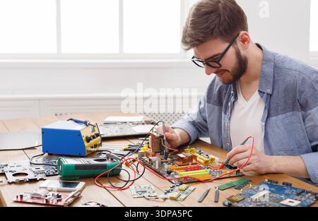 Man Works on Electronic Circuit Boards at a Table in a Bright Room With Tools Nearby Stock Photo