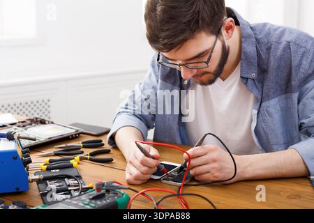 Young Man Repairing a Device With Tools on a Wooden Table in a Bright Room Stock Photo