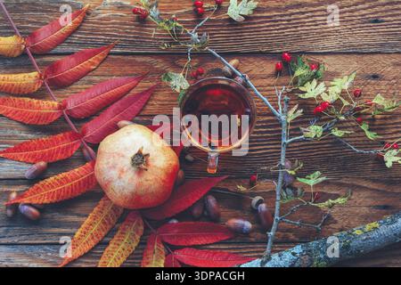 Autumn still life of colorful leaves, a Cup of tea, pomegranate, acorns and a branch with wild rose berries on an old brown wooden table, top view Stock Photo