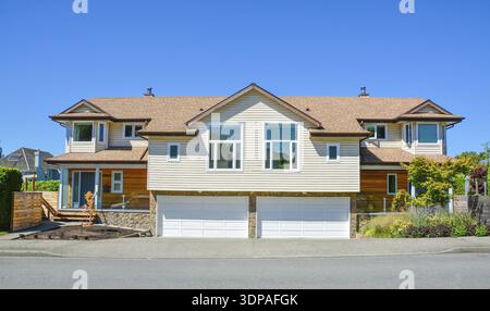 Brand new residential duplex house for two families. House for sale on blue sky background. Duplex house with wide garage doors along the road in the Stock Photo
