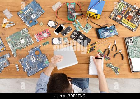 Worker Repairs Electronics on a Wooden Table With Circuit Boards and Tools in a Workshop Stock Photo