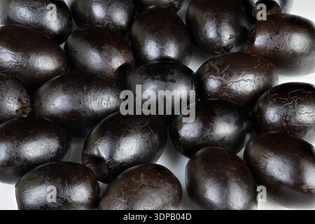 Shiny black olives piled closely on white background, glossy brine sheen, pitted surfaces, chef ingredient for Mediterranean recipes, styled for culin Stock Photo