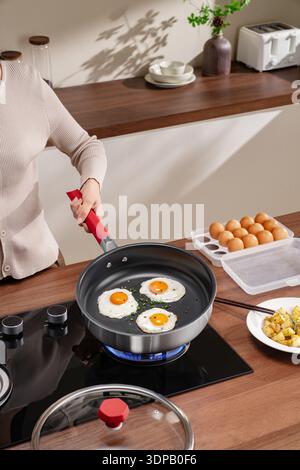 Woman frying three sunny side up eggs in non-stick pan for breakfast Stock Photo