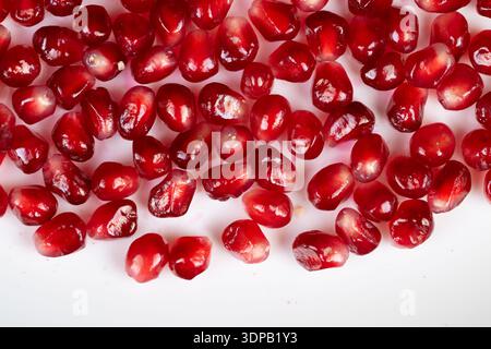 Bright pomegranate seeds scattered on white surface, highcontrast closeup showcasing glossy ruby arils with crisp studio lighting ideal for food packa Stock Photo