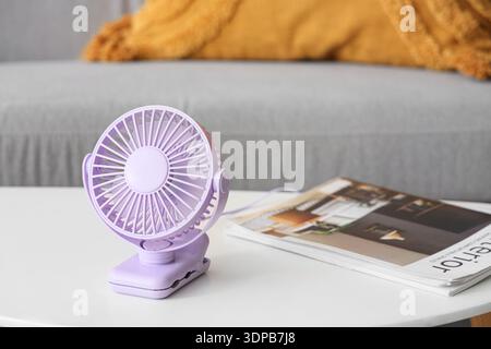 Lilac mini fan with magazine on table in living room, closeup Stock Photo