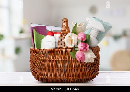Basket with cleaning supplies and flowers on table in kitchen. Spring cleaning Stock Photo