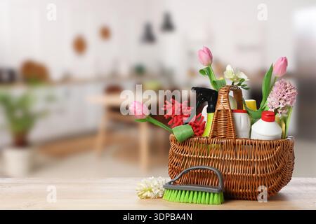 Basket with cleaning supplies and flowers on table in kitchen. Spring cleaning Stock Photo