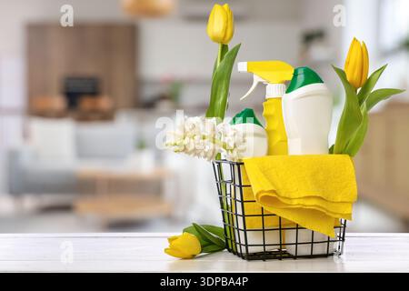 Basket with cleaning supplies and flowers on table in kitchen. Spring cleaning Stock Photo