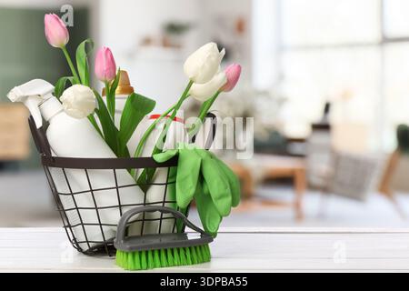 Basket with cleaning supplies and flowers on table in room. Spring cleaning Stock Photo