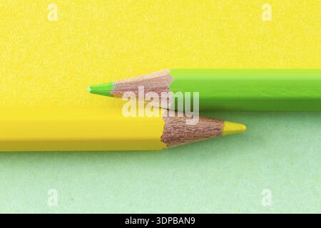 Yellow and green color pencils on yellow and green background color papers arranged horizontally. Minimalist composition Stock Photo