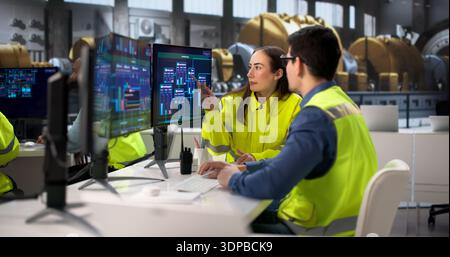Engineers Operating Multiple Screens At Power Plant In Desktop Computer. Young Operator Using System In Diverse Group Stock Photo