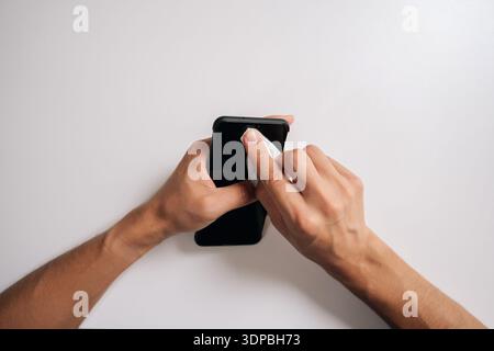 Top view of unrecognizable man cleaning screen of smartphone with disinfectant wipe, promoting hygiene and effectively eliminating germs and bacteria Stock Photo