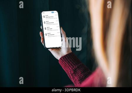 Over-the-shoulder view of a woman holding a smartphone displaying an email inbox. Modern lifestyle scene with copy space, ideal for business communica Stock Photo