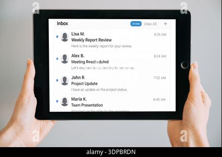 Close-up of hands holding a digital tablet displaying an email inbox interface with business messages. Modern communication, remote work, and mobile p Stock Photo