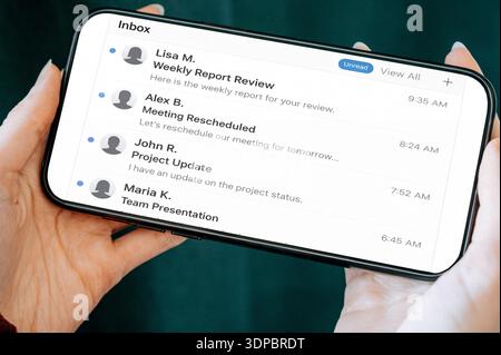 Close-up of hands holding a smartphone displaying an email inbox with business messages and unread notifications. Modern mobile communication, remote Stock Photo
