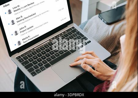 Close-up of a woman reviewing email inbox on laptop in a home office setting. Modern remote work, online communication, productivity and business work Stock Photo