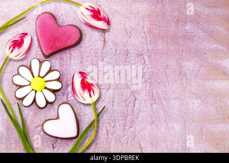 Red - white flowers tulips and gingerbread cookies in the shape of a heart and a camomile on a pastel pink aged wooden background. Place for text. Vie Stock Photo