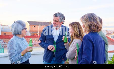 Group of friends socializing on rooftop party enjoying drinks Stock Photo