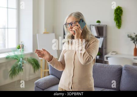 Old senior woman talking on phone at home, gesturing for family, friend, doctor communication  Stock Photo