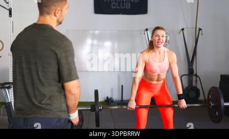 Woman lifting barbell with trainer in gym Stock Photo