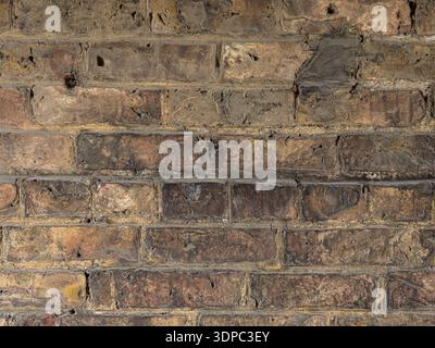 Darkened aged brick wall with uneven coloration and worn industrial character. Stock Photo
