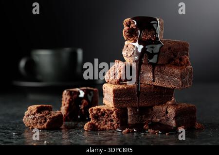 Brownie pieces on a black background. Melted chocolate drips down the brownie. Copy space. Stock Photo