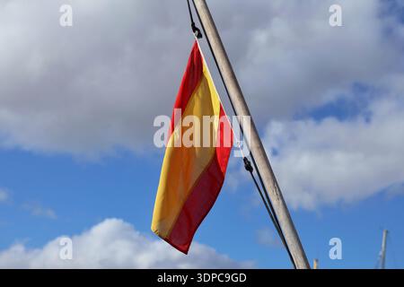 A Spanish flag hangs on a pole and waves under a blue sky with white clouds Stock Photo