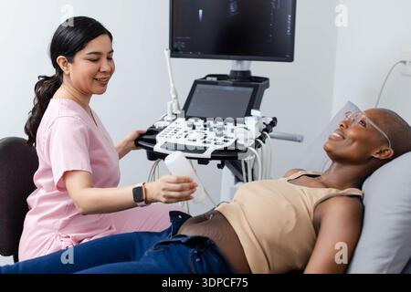 Asian tech in scrubs holding gel using ultrasound African American female patient lying on exam bed Stock Photo