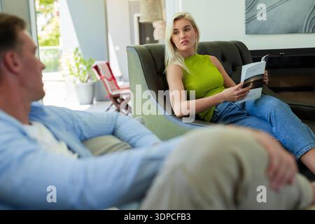 Couple sitting in living room, woman wearing green top holding magazine, man reclining Stock Photo