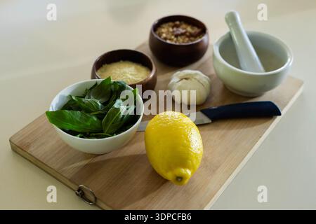 Whole lemon sitting on wooden cutting board with basil, paring knife, garlic, mortar Stock Photo