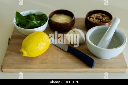 Whole lemon is sitting on cutting board on countertop, with knife, basil, grated cheese and mortar Stock Photo