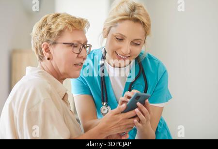 Nurse shows smartphone to elderly patient during medical consult in clinic Stock Photo