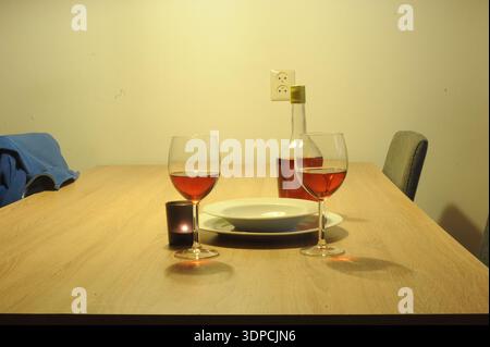 Romantic dinner setup featuring two wine glasses, a bottle of rosé, a lit candle and plates on a wooden table creating an intimate, cozy atmosphere. Stock Photo