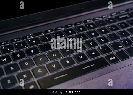 A person types on a laptop keyboard in a dark room. The focus is on the keys and layout of the keyboard. Stock Photo