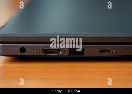 A laptop is placed on a wooden table showing various ports for connecting devices and accessories. The view highlights technology. Stock Photo