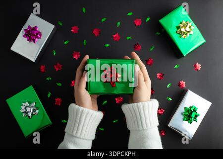 Dive into holiday magic! First person top view of hands reach for lavish silver giftbox featuring bow, on black backdrop. Perfect for xmas party Stock Photo
